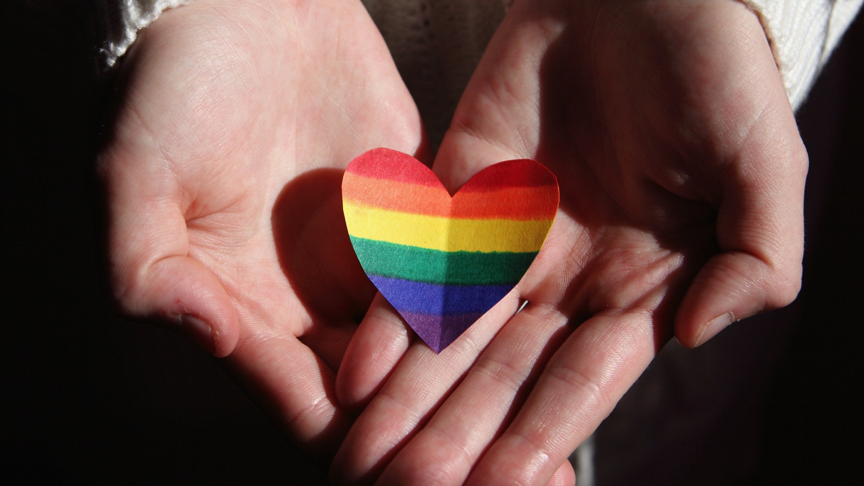 Hands holding paper rainbow heart